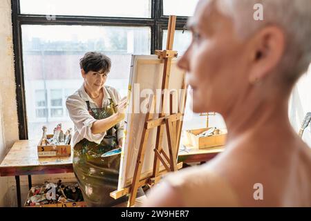 skilled female artist painting portrait on blurred mature model in craft workshop, inspiration Stock Photo