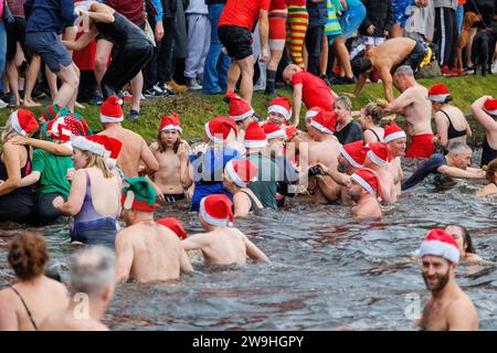 The annual Christmas morning dip into Blackroot Pool in Sutton Coldfield Park. On the stroke of 10am, people dressed in festive costumes, dive, jump, lower themselves into the water. Stock Photo