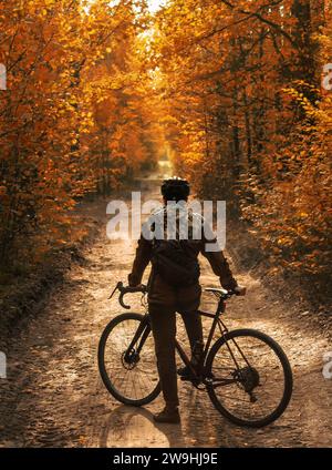 A cyclist stands on a path in a beautiful autumn forest with orange leaves in daylight. Beautiful autumn landscape. Active lifestyle. Stock Photo
