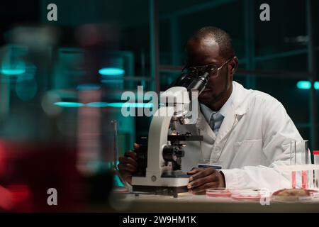 African american scientist sitting at his workplace in laboratory working with microscope Stock Photo