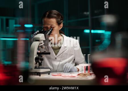 Young asian lab assistant looking through microscope conducting scientific research Stock Photo