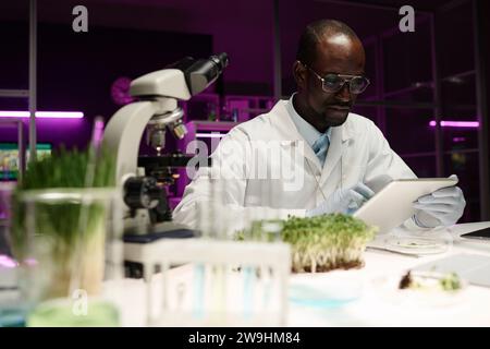 Biologist reading information on digital tablet screen sitting at his desk in laboratory Stock Photo