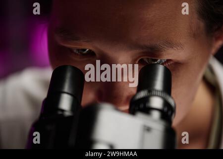 Extreme closeup of eyes of asian researcher attentively looking through microscope Stock Photo
