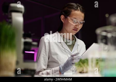 Young asian female researcher using digital tablet sitting at her workplace in laboratory Stock Photo