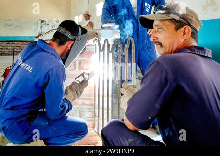 Cuban people working: A welder works on a metal part while another helps him by holding it still in place. Stock Photo