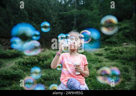 Toddler girl blowing soap bubbles in beautiful green summer nature. Stock Photo