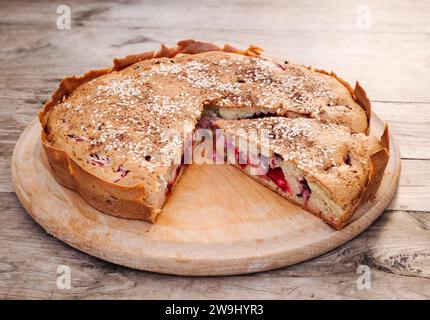 Rustic homemade cherry and cherry plum pie sprinkled with sesame seeds on a round cutting board on an old wooden table. Country style. Stock Photo