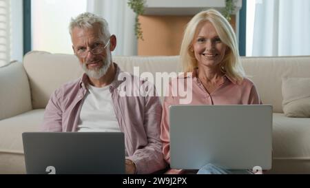 Happy Caucasian elderly married couple senior man woman retired businesspeople business work on Internet together in living room using laptops smiling Stock Photo