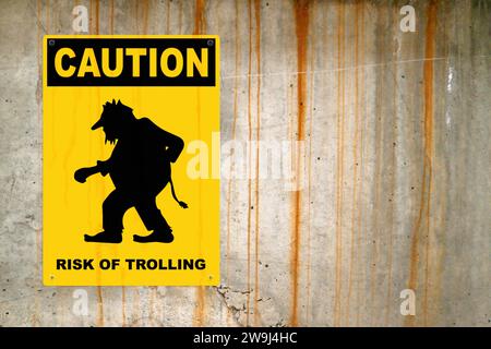 Yellow warning sign screwed to a concrete wall to warn about a threat. In the middle of the panel, there is a Troll symbol and the message is saying ' Stock Photo
