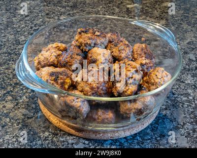 Shimmering golden-brown meatballs grace a glass bowl, poised atop a dark, polished granite countertop. Stock Photo