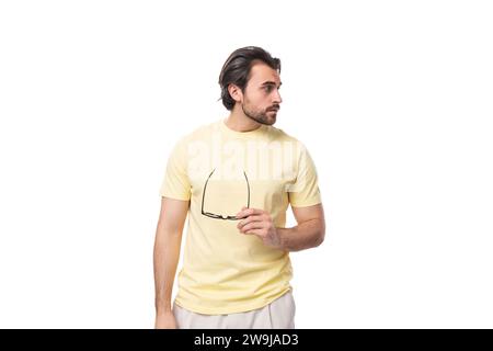 a young smart brunette man with a black beard and mustache stands thoughtfully taking off his glasses Stock Photo