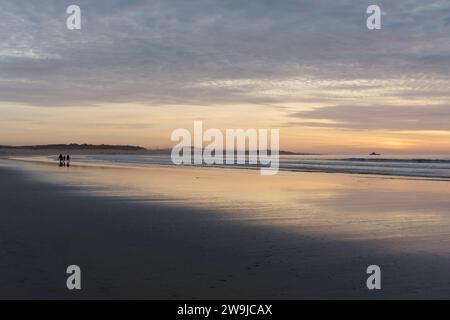 Family in silhouette walk on a wet sandy beach at sunset with a windfarm behind, in the city of Essaouira, Morocco. December 28, 2023 Stock Photo