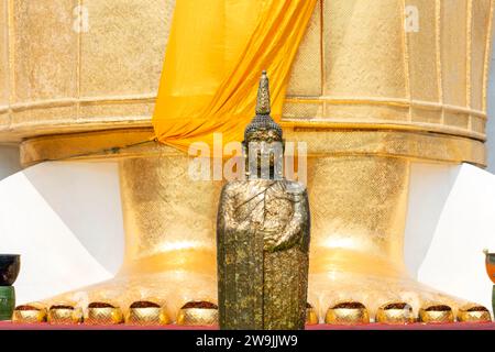 Buddha figure decorated with gold leaf in front of a 32 metre high standing Buddha statue, Wat Intharawihan, Bangkok, Thailand Stock Photo