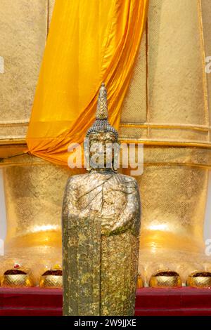 Buddha figure decorated with gold leaf in front of a 32 metre high standing Buddha statue, Wat Intharawihan, Bangkok, Thailand Stock Photo