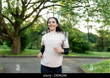 Young beautiful woman running in the evening in the park, hispanic woman with curly hair smiling contentedly, active lifestyle Stock Photo