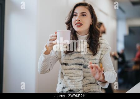 Young woman discussing ideas in a modern office kitchen with her teammates over a tea early in the morning. Stock Photo