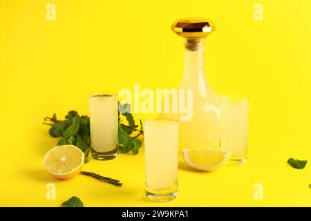 Bottle and shots of tasty Limoncello with mint on yellow background Stock Photo