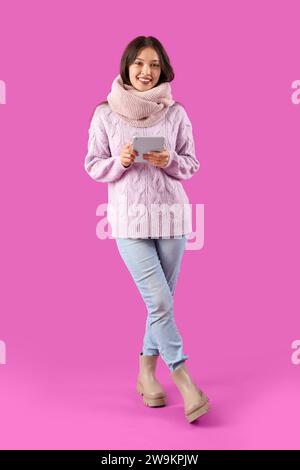 Beautiful young Asian woman in warm scarf with tablet on purple background Stock Photo