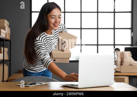 Female Asian seller with shoe boxes using laptop in warehouse store Stock Photo