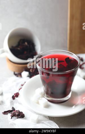 Aromatic hibiscus tea in glass, dried roselle calyces and sugar cubes on light table Stock Photo