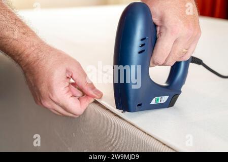 Worker stapling sofa lining with electric staple gun Stock Photo