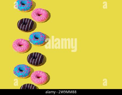 Creative arrangement of colorful donuts on light yellow background with copy space. Minimal food concept. Trendy yummy donuts idea. Donuts aesthetic. Stock Photo