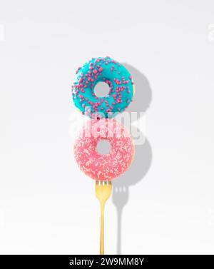 Yummy pink and blue glazed donuts with sprinkles pricked on a fork on white background. Creative art. Contemporary style. Minimal food concept. Stock Photo
