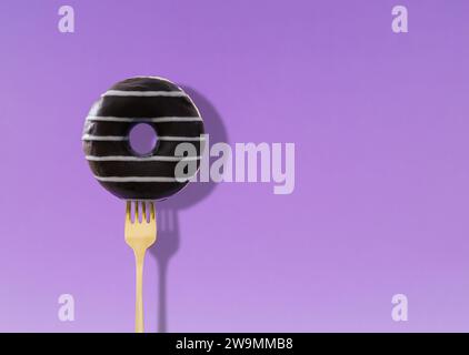 Yummy donut pricked on a fork on light violet background. Creative art. Contemporary style. Minimal concept of food with copy space for text. Stock Photo