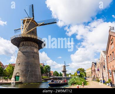 A tour boat cruising at the foot of the Schiedam windmills near Rotterdam, Netherlands, the tallest classic windmills in the world. Stock Photo
