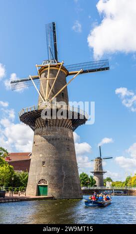 A tour boat cruising at the foot of the Schiedam windmills near Rotterdam, Netherlands, the tallest classic windmills in the world. Stock Photo