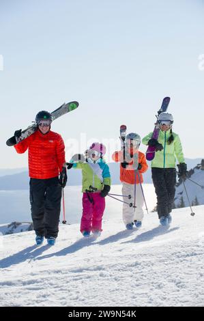 A family of four skiers walks with their skis over their shoulders at the top of Alpine Meadows ski resort on the north shore of Lake Tahoe, California. Stock Photo