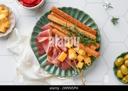 Slices of prosciutto or jamon. Antipasto. Delicious grissini sticks with prosciutto, cheese, rosemary, olives on green plate on white concrete backgro Stock Photo