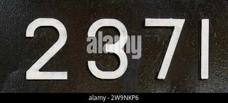 Weathered numbers two, three, seven, one, 2371 or 2, 3, 7, 1 painted white on a piece of black metal. Abstarct numeral background for design. Stock Photo
