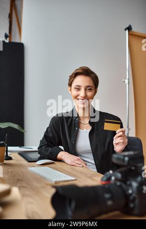 jolly attractive female photographer paying online using her credit card and smiling at camera Stock Photo