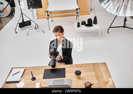 attractive professional female photographer in casual attire working with her camera in studio Stock Photo