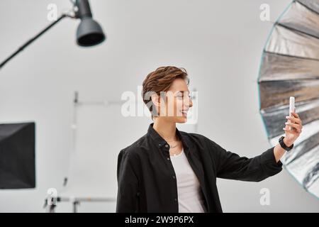 jolly charming woman with in casual attire with short hair making stories for social media in studio Stock Photo