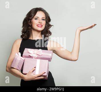 Brunette woman showing pink present gift box holding empty palm hand standing against white studio wall background. Holidays, celebration and women co Stock Photo