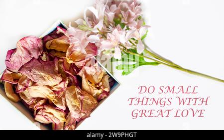Quote Do small things with great love written in calligraphy style on paper with pink rose petals in a box and a sprig of flowers Stock Photo