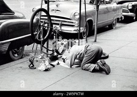 Man fixing bicycle on sidewalk, New York City, New York, USA, Angelo Rizzuto, Anthony Angel Collection, May 1954 Stock Photo