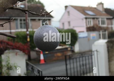 A close up photo of a red Christmas bauble hanging from a tree branch outside. Stock Photo