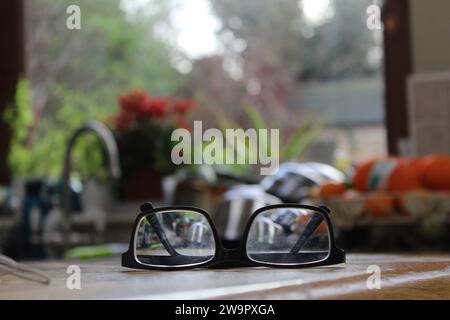 A close up of a pair of black glasses on a wooden surface in a kitchen interior. Stock Photo