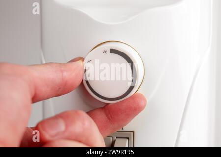 Hand turning the radiator thermostat of home electric oil heater increasing the temperature close up Stock Photo