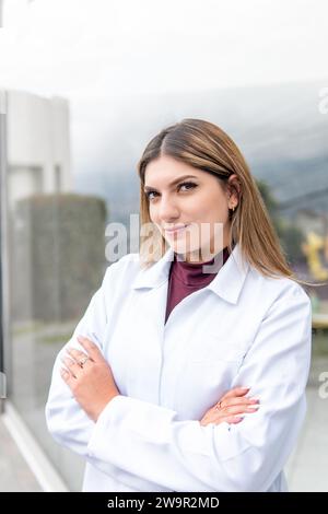 Portrait of a young Latina female doctor looking at camera in front of a hospital window. Health concept Stock Photo