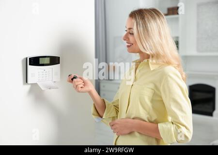 Home security system. Smiling woman using alarm key fob in room Stock Photo