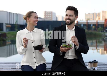 Smiling business people eating from lunch boxes outdoors Stock Photo