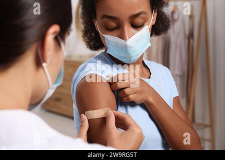 Doctor putting adhesive bandage on young woman's arm after vaccination indoors Stock Photo