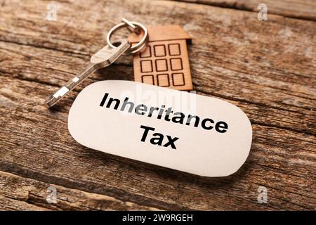 Inheritance Tax. Card and key with key chain in shape of house on wooden table, closeup Stock Photo