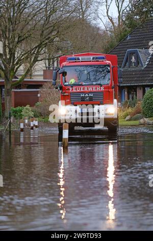 Borgfeld, Germany. 30th Dec, 2023. A fire department emergency vehicle drives through a flooded street in Borgfeld near Bremen. The river Wümme has burst its banks here. Credit: Markus Hibbeler/dpa/Alamy Live News Stock Photo