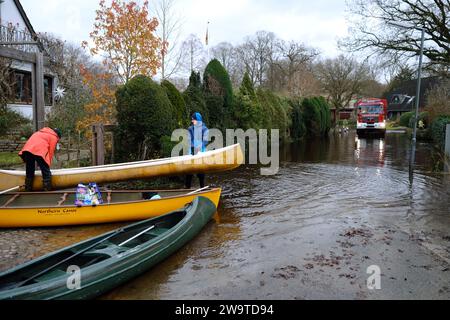 Borgfeld, Germany. 30th Dec, 2023. Two young people carry a canoe along a flooded street in Borgfeld near Bremen. The river Wümme has burst its banks here. Residents can only reach their homes by boat. Credit: Markus Hibbeler/dpa/Alamy Live News Stock Photo