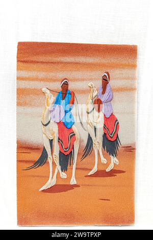 A sand painting in relief drawing of two tuareg people wearing traditional clothes and head scarfs riding white dromedary camels walking on the Sahara Stock Photo